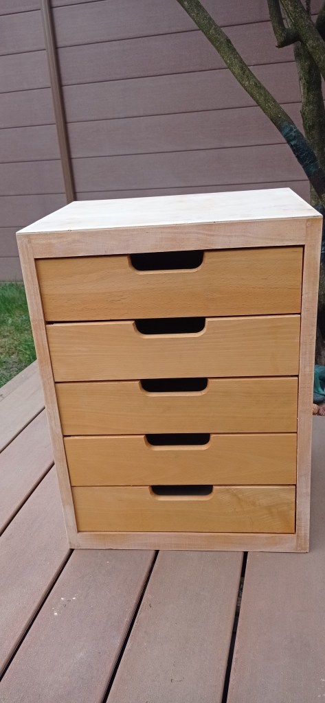 A wooden drawer unit with four drawers, shown on a wooden surface outdoors.