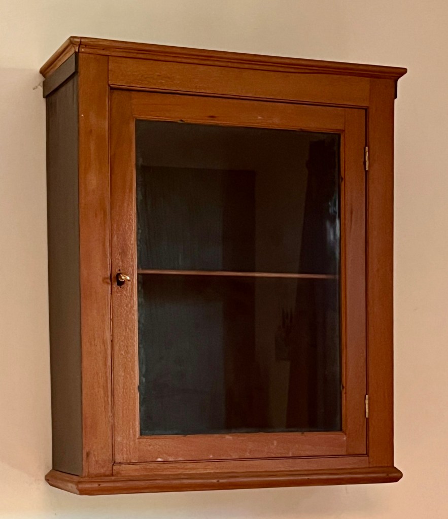 A wooden wall cabinet with a glass door, displaying a simple and elegant design.