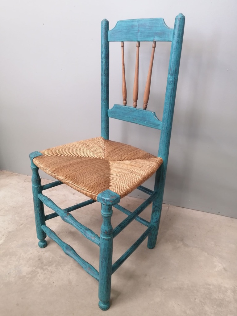 A turquoise wooden chair with a woven straw seat, featuring vertical slats on the backrest.