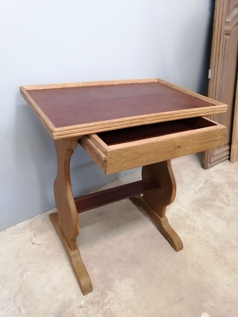 A wooden table with a brown leather top and a single drawer, situated against a light blue wall.