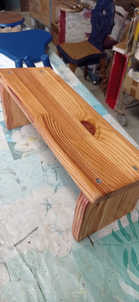 A wooden shelf or stand made of pine, featuring a smooth, polished top and rounded edges, displayed on a colorful work table in a workshop.