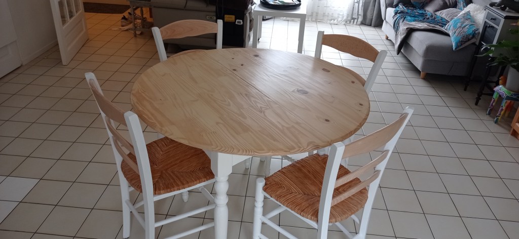 Round wooden dining table with four white chairs on a tiled floor in a cozy living space.
