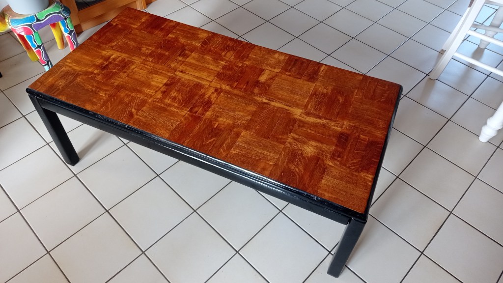 Coffee table with a wooden top featuring a geometric pattern, set on a black frame, placed on tiled floor.