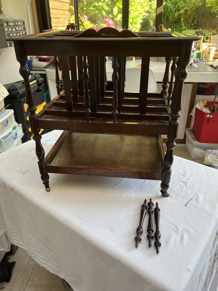 A wooden table frame with turned legs, placed on a white tablecloth. Four decorative legs are detached and resting beside it.