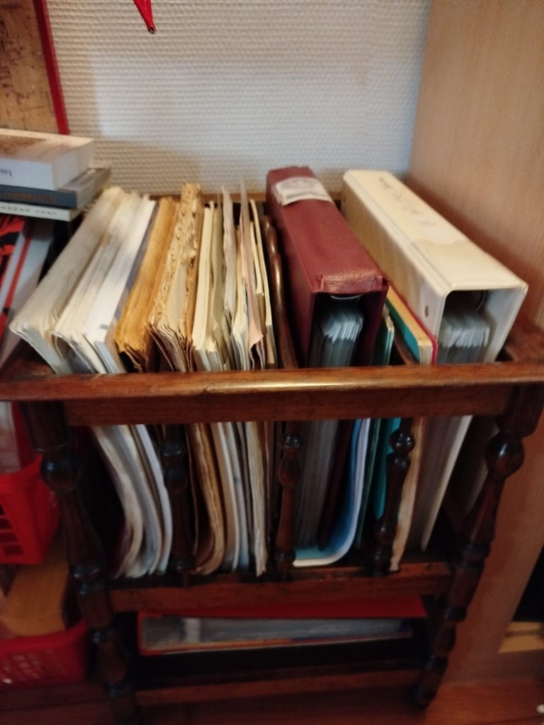 A wooden magazine rack holding various folders and files, some with visible wear and age, alongside a few stacked boxes.