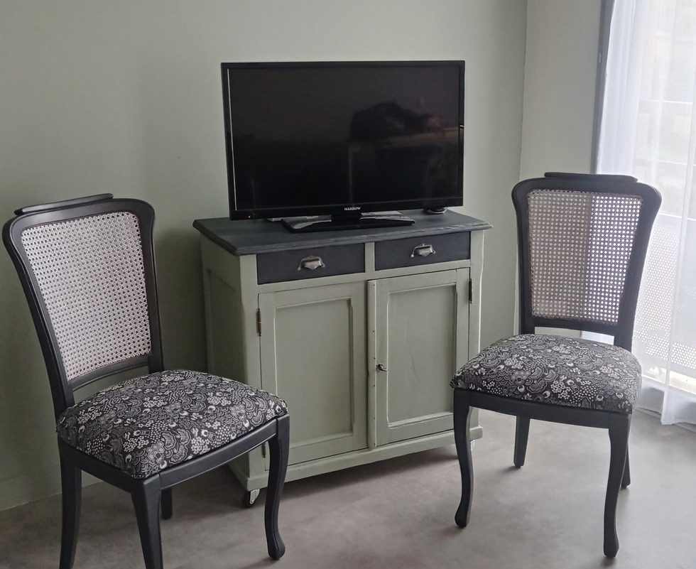 Living room setup featuring a television on an antique-style cabinet with two patterned chairs on either side.