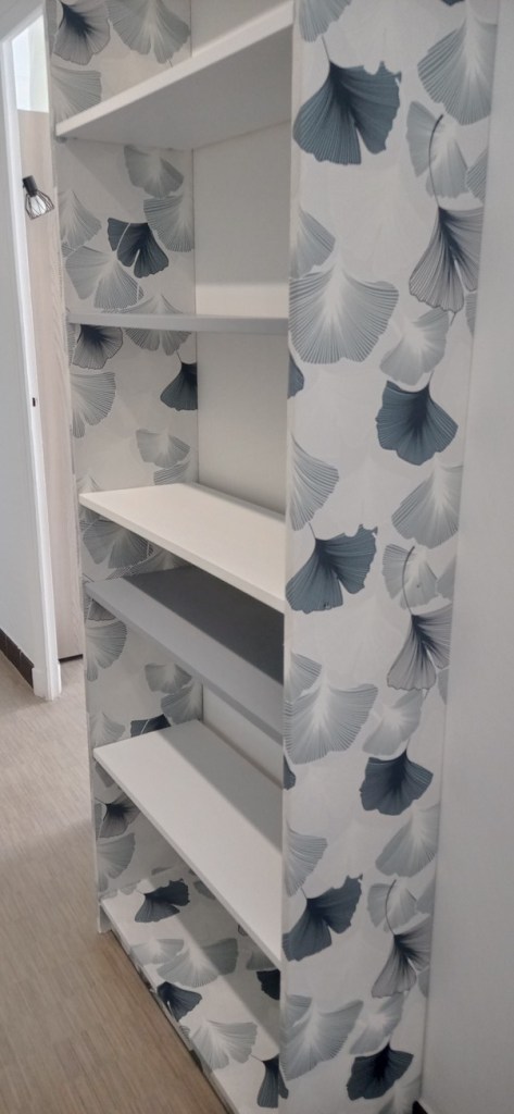 A white bookshelf with open shelves, featuring a decorative background of blue and gray ginkgo leaf patterns.